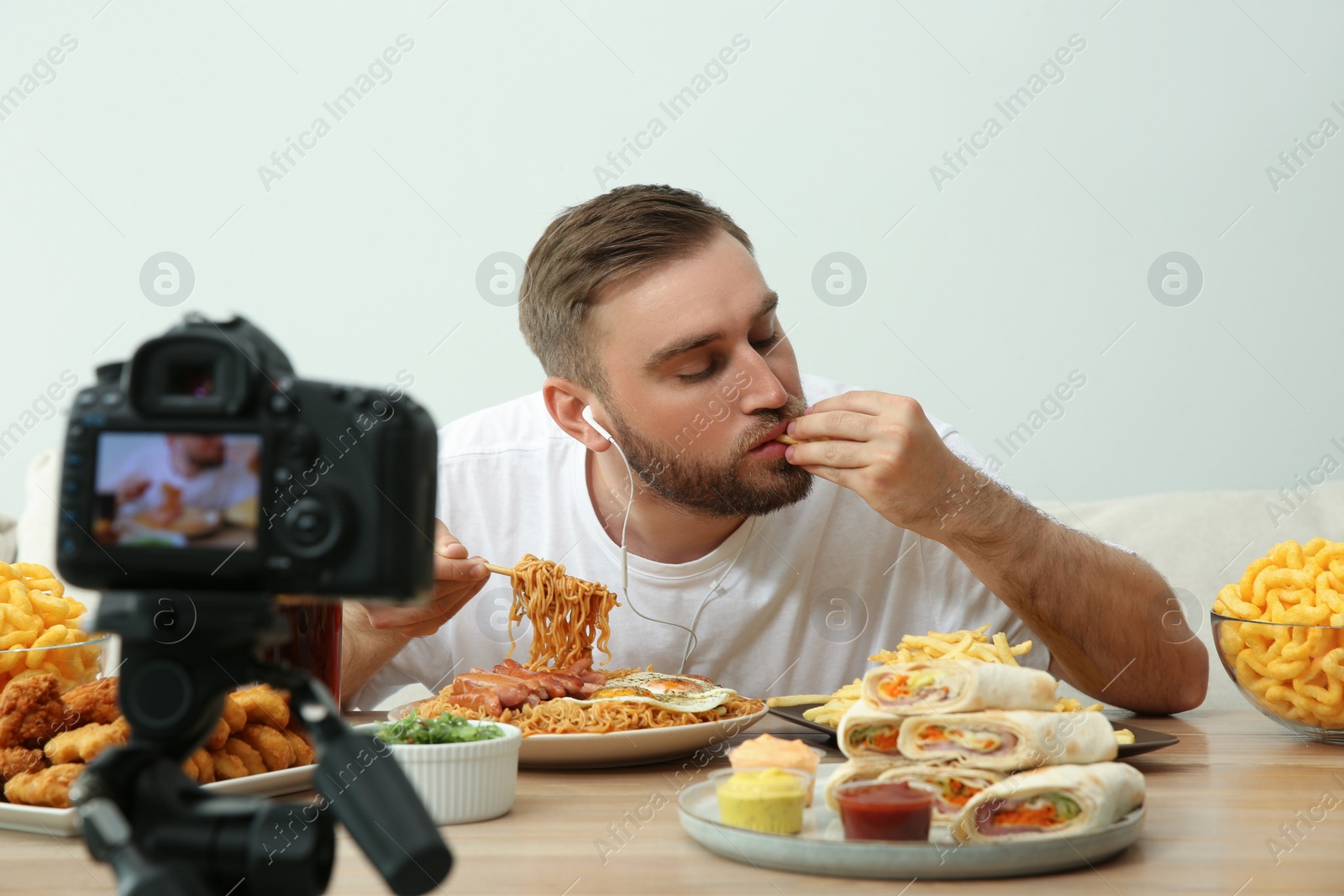 Photo of Food blogger recording eating show on camera against light background. Mukbang vlog