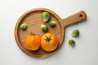 Photo of Cutting board with Brussels sprouts and tomatoes on white wooden table, top view