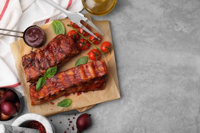 Photo of Tasty roasted pork ribs served with sauce, basil and tomatoes on grey table, flat lay. Space for text