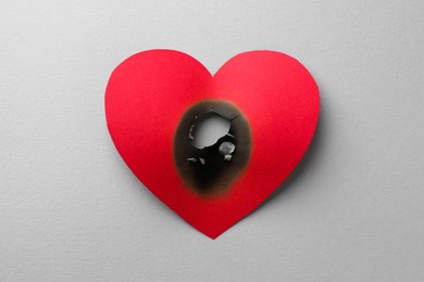Photo of Red paper heart with burnt hole on white background, top view. Broken heart
