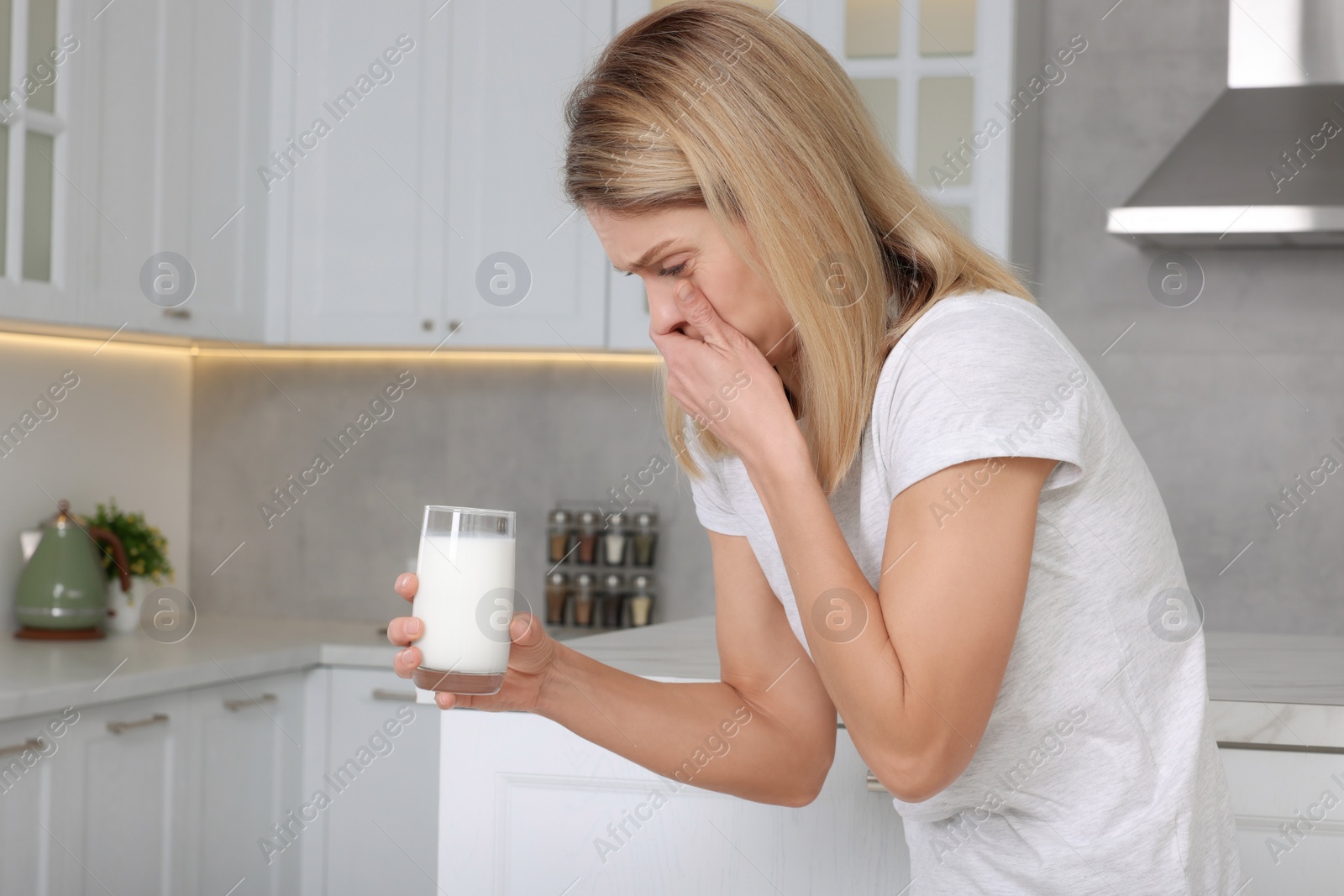 Photo of Woman with glass of milk suffering from lactose intolerance in kitchen, space for text