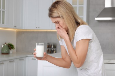 Woman with glass of milk suffering from lactose intolerance in kitchen, space for text