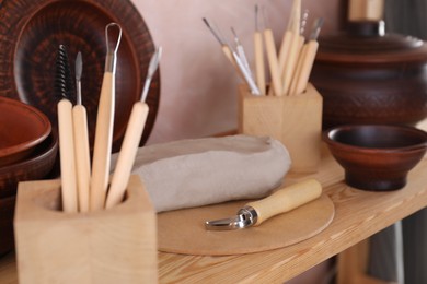 Set of different crafting tools and clay dishes on wooden rack in workshop, closeup