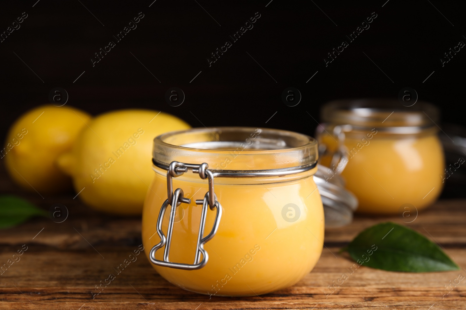 Photo of Delicious lemon curd in glass jar on wooden table