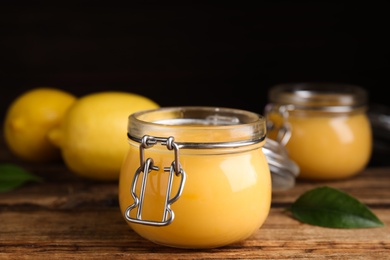 Photo of Delicious lemon curd in glass jar on wooden table