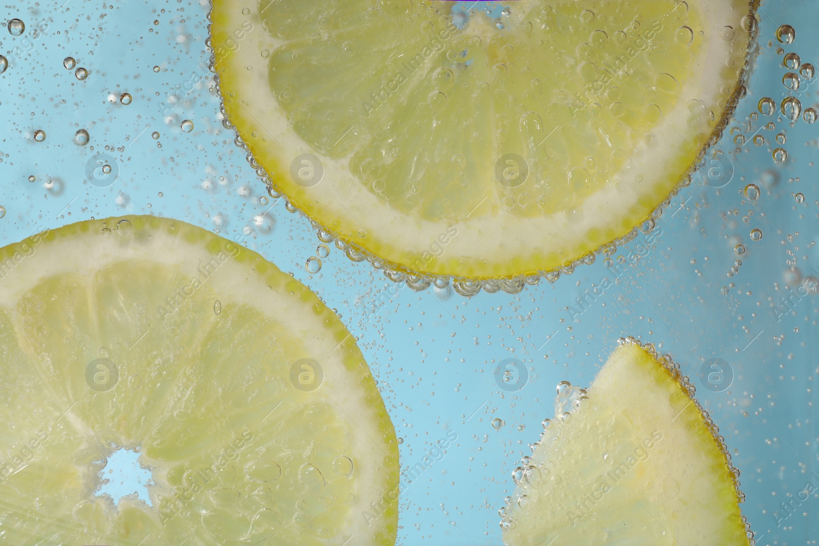 Photo of Juicy lemon slices in soda water against light blue background, closeup