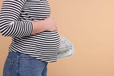 Surrogate mother. Pregnant woman with dollar banknotes on beige background, closeup. Space for text