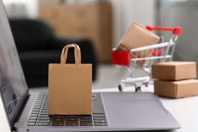 Photo of Online store. Small shopping bag and laptop on table, closeup