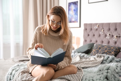 Photo of Young woman reading book on bed at home