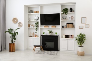 Photo of Stylish room interior with beautiful fireplace, TV set and shelves with decor and houseplants