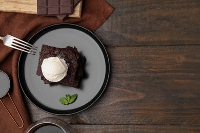 Tasty brownies served with ice cream on wooden table, flat lay. Space for text