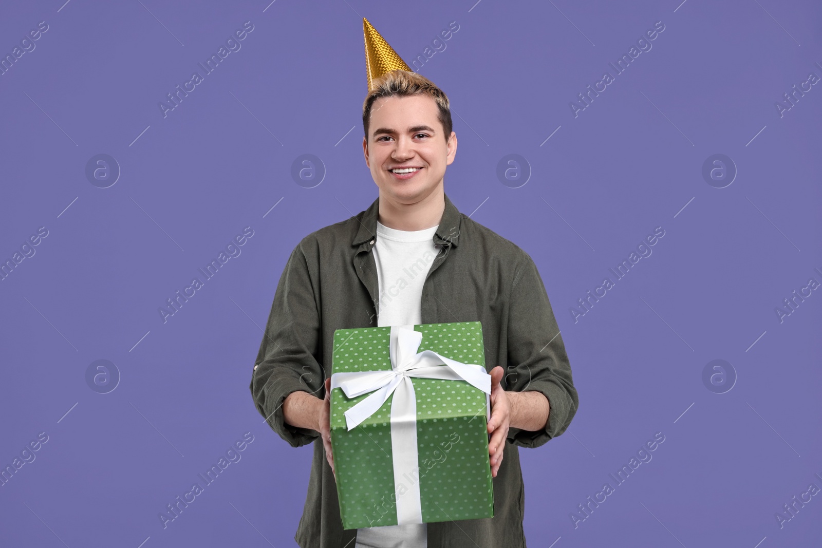 Photo of Young man with party hat and gift box on purple background