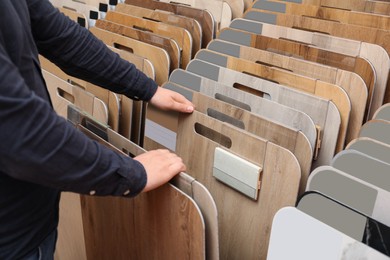 Photo of Man choosing wooden flooring among different samples in shop, closeup