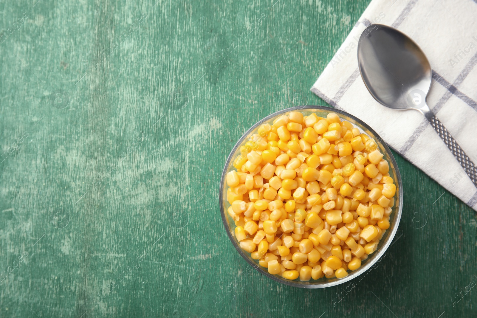 Photo of Bowl with corn kernels on green wooden background, top view. Space for text