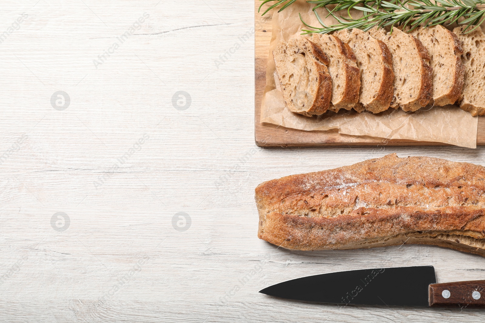 Photo of Buckwheat baguettes with knife and rosemary on white wooden table, flat lay. Space for text