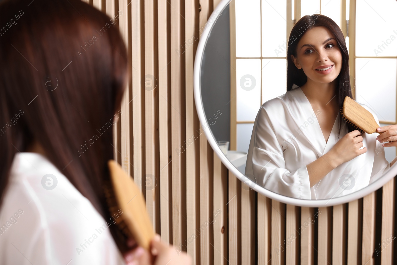 Photo of Beautiful woman brushing her hair near mirror in room