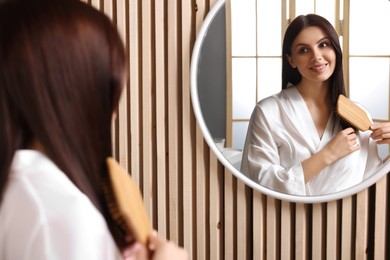 Photo of Beautiful woman brushing her hair near mirror in room