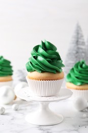 Photo of Delicious cupcakes with green cream and Christmas decor on white marble table