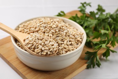 Photo of Dry pearl barley in bowl and wooden spoon on table, closeup