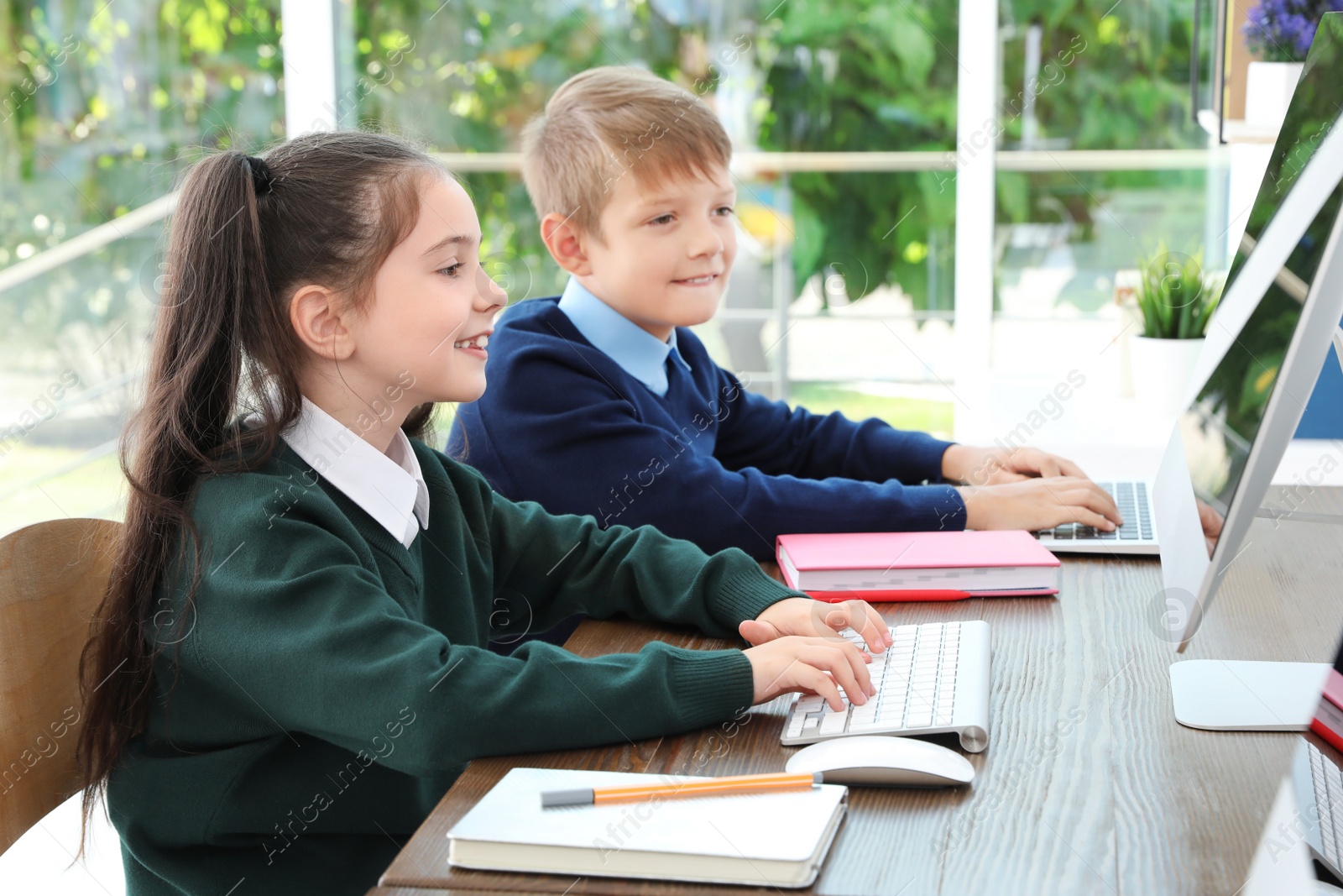 Photo of Little children in stylish school uniform at desks with computers