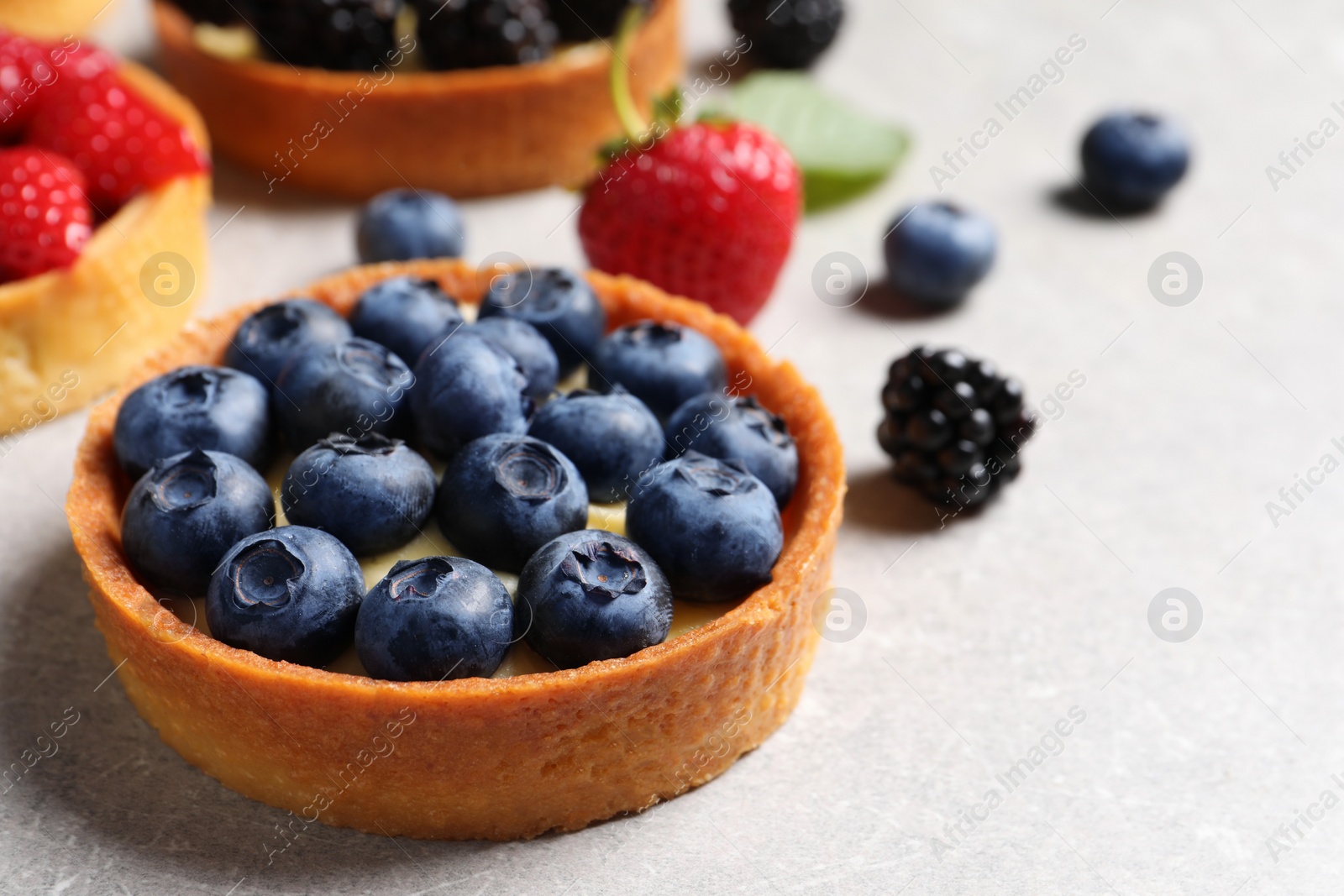 Photo of Tartlet with fresh blueberries on light grey table, closeup and space for text. Delicious dessert