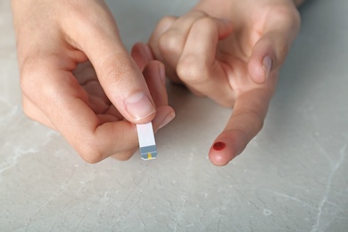 Photo of Woman with blood sugar test stripe at table. Diabetes control