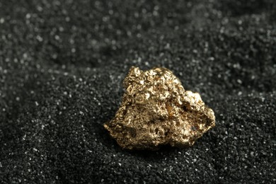 Photo of Shiny gold nugget on black sand, closeup. Space for text