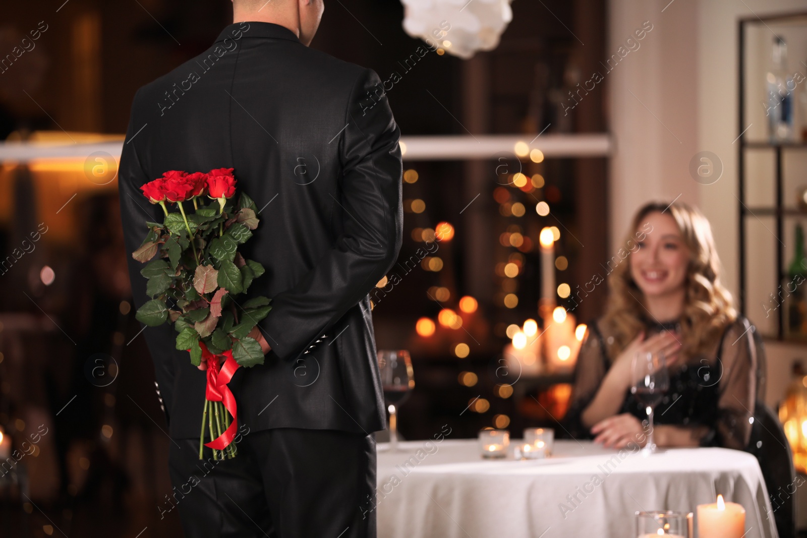 Photo of Man hiding roses for his beloved woman in restaurant at Valentine's day dinner