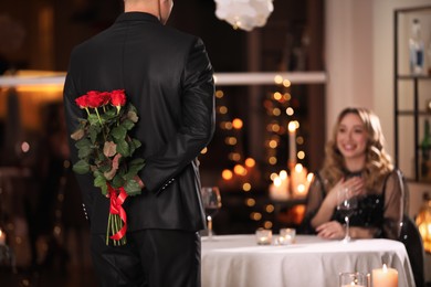 Man hiding roses for his beloved woman in restaurant at Valentine's day dinner