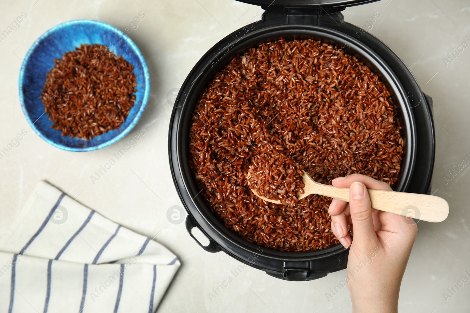 Photo of Woman taking delicious brown rice from multi cooker at table, top view