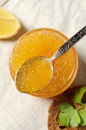 Photo of Fresh pike caviar in glass jar, bread, parsley and lemon on table, flat lay