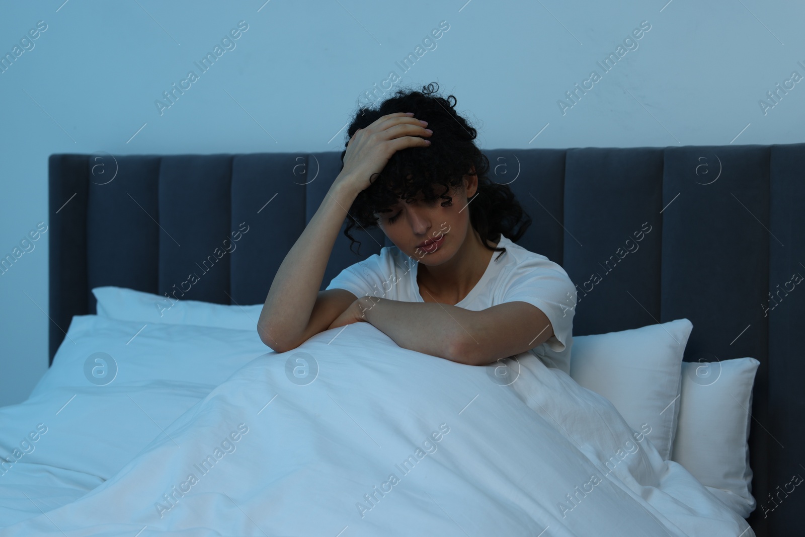 Photo of Young woman suffering from headache in bed at night