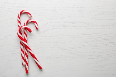 Photo of Candy canes on white wooden background, flat lay with space for text. Traditional Christmas treat