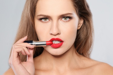 Photo of Young woman applying red lipstick on gray background