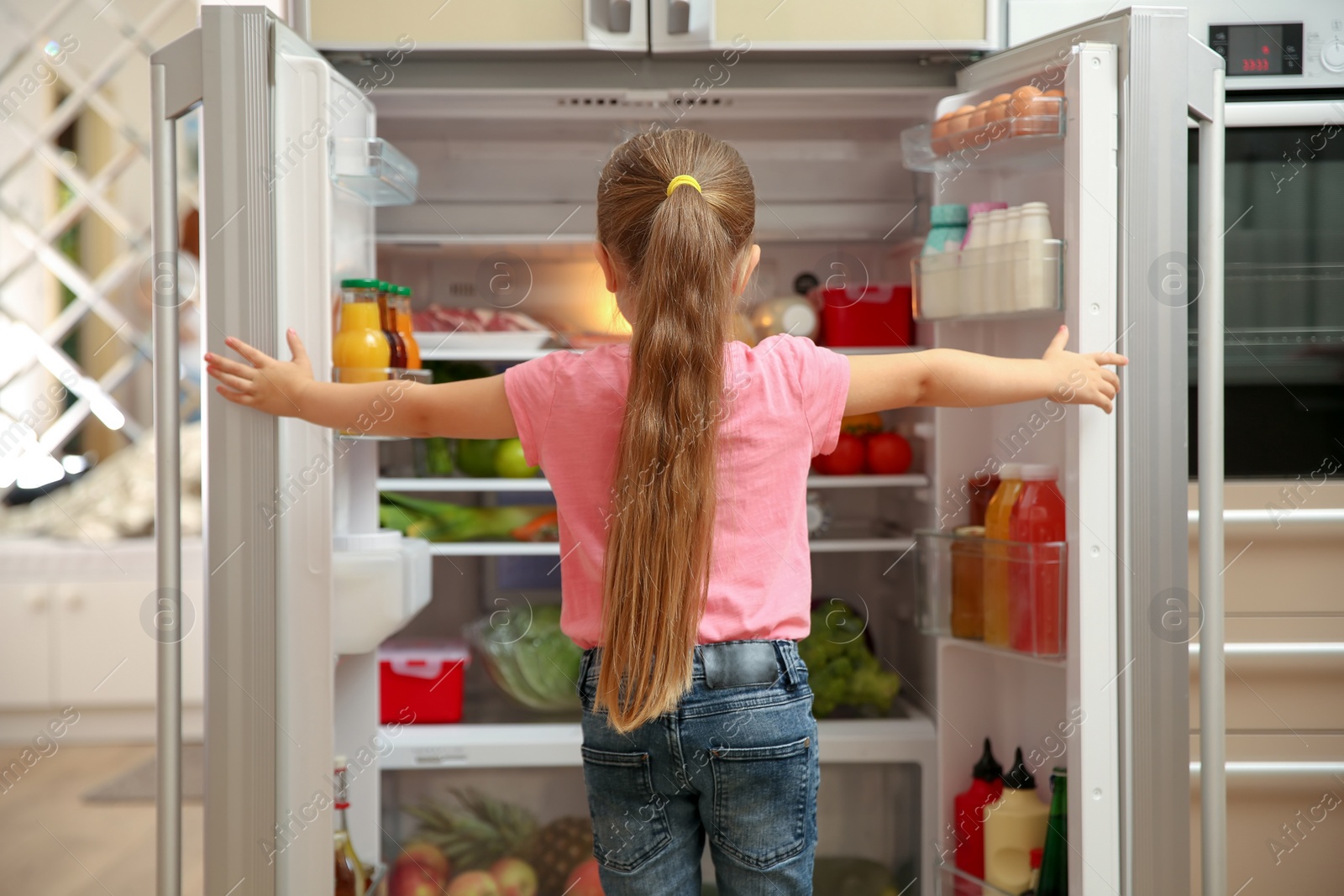 Photo of Cute little girl choosing food in refrigerator at home