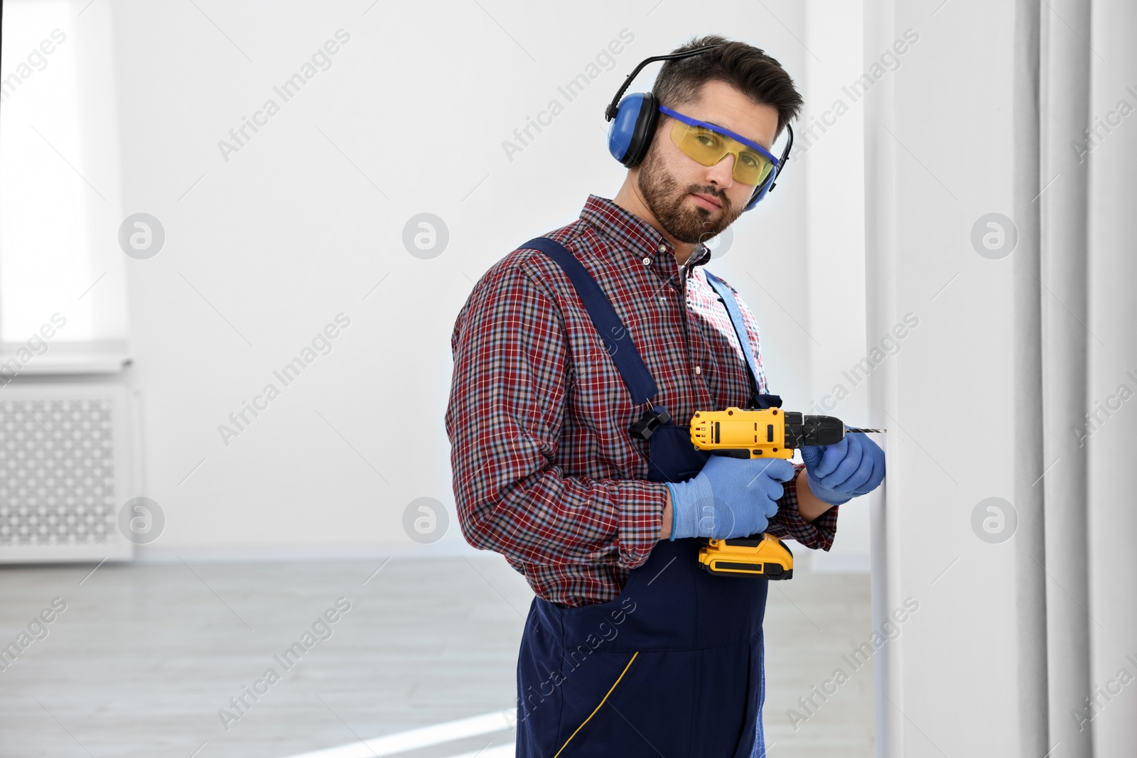 Photo of Young worker in uniform using electric drill indoors, space for text