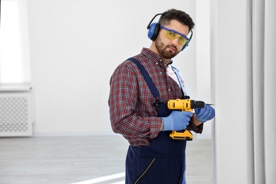 Photo of Young worker in uniform using electric drill indoors, space for text