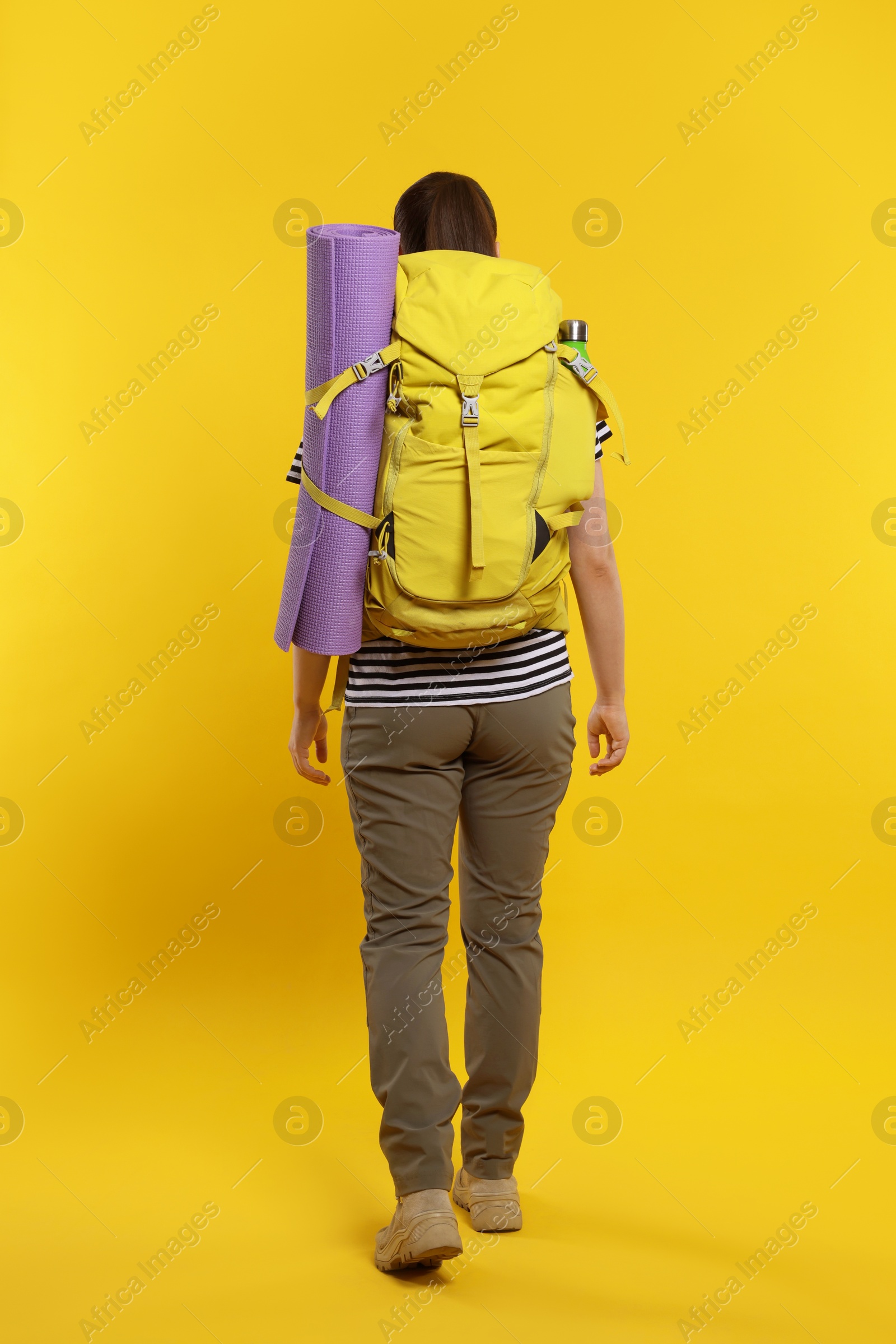 Photo of Woman with backpack walking on orange background, back view. Active tourism