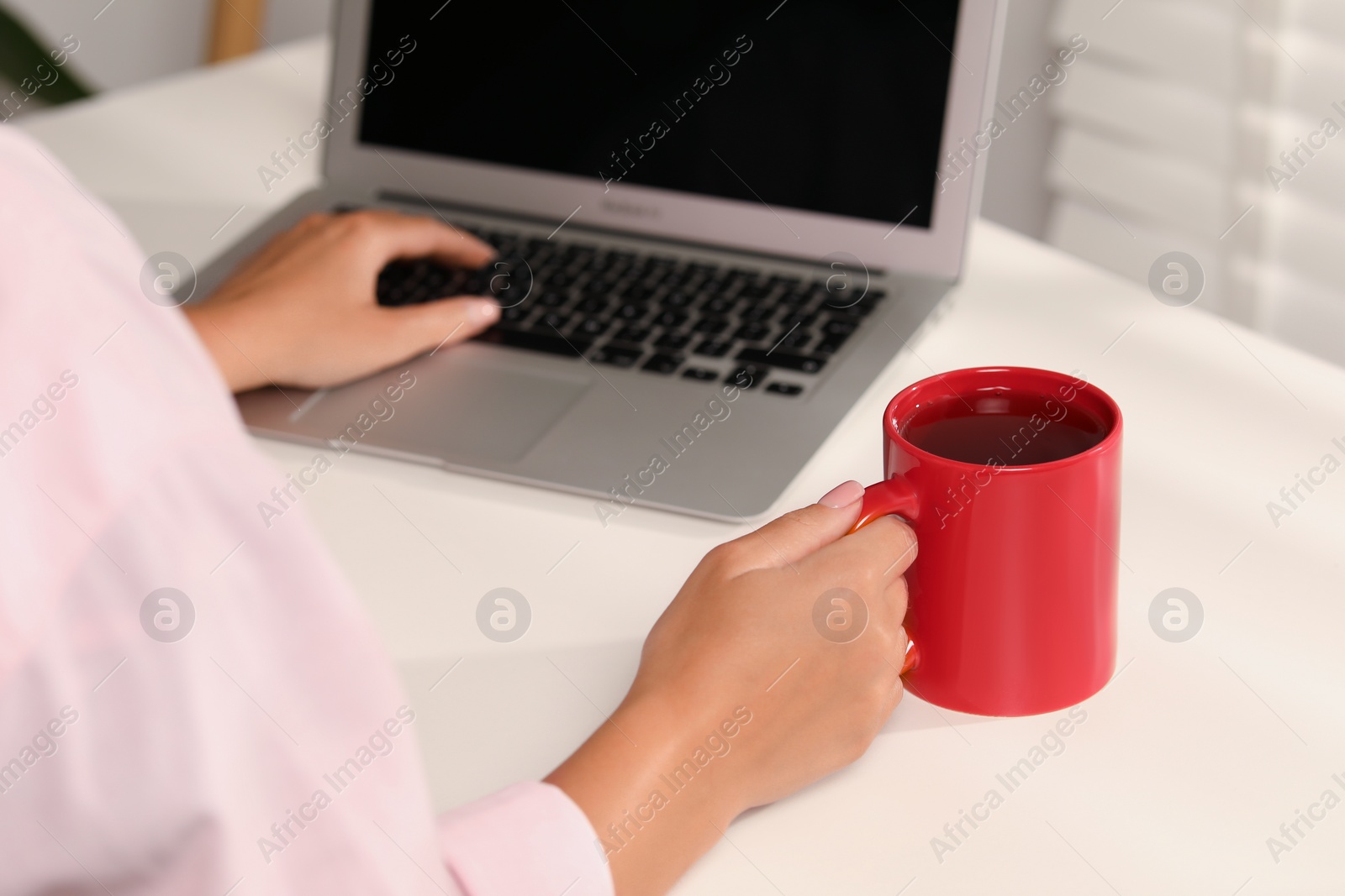 Photo of Woman with red ceramic mug at workplace, closeup