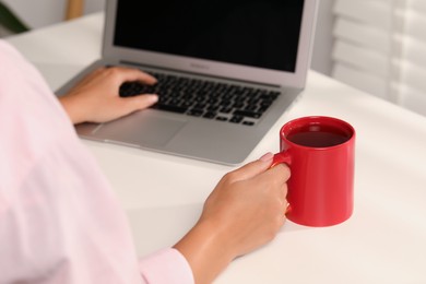 Photo of Woman with red ceramic mug at workplace, closeup