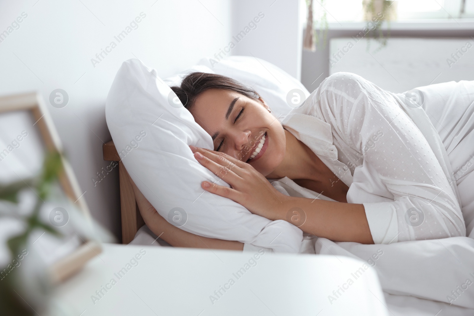 Photo of Happy young woman lying on soft pillow in bed at home