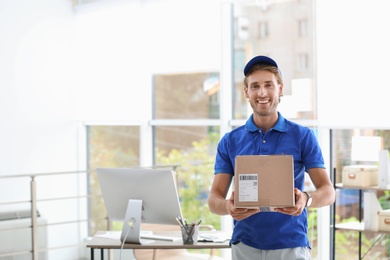 Photo of Young courier standing with parcel near office desk. Space for text