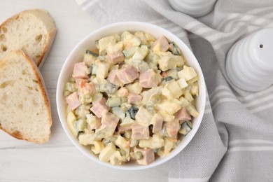 Photo of Tasty Olivier salad with boiled sausage in bowl and bread on white wooden table, flat lay
