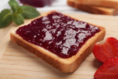 Photo of Toast with tasty jam and cut strawberry on wooden board, closeup