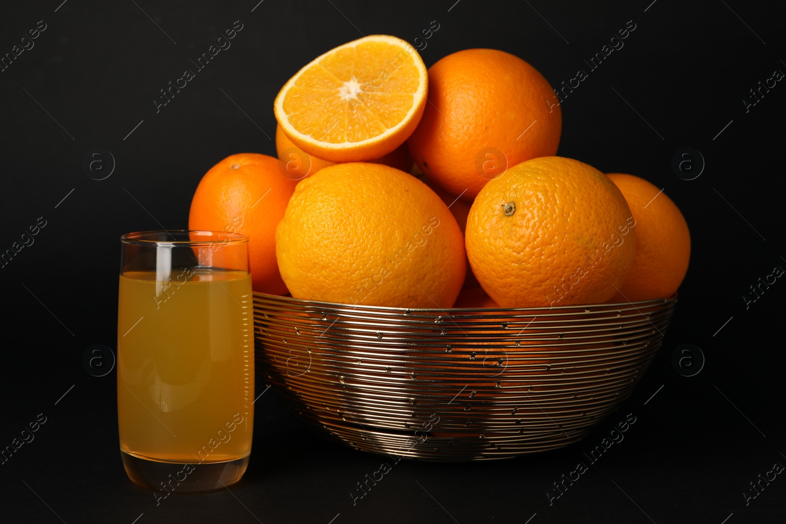 Photo of Bowl with ripe oranges and fresh juice on black background