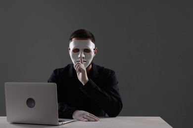 Photo of Man in mask and gloves sitting with laptop and showing hush gesture at white table against grey background. Space for text