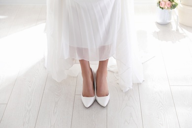 Young bride wearing beautiful wedding shoes indoors, closeup