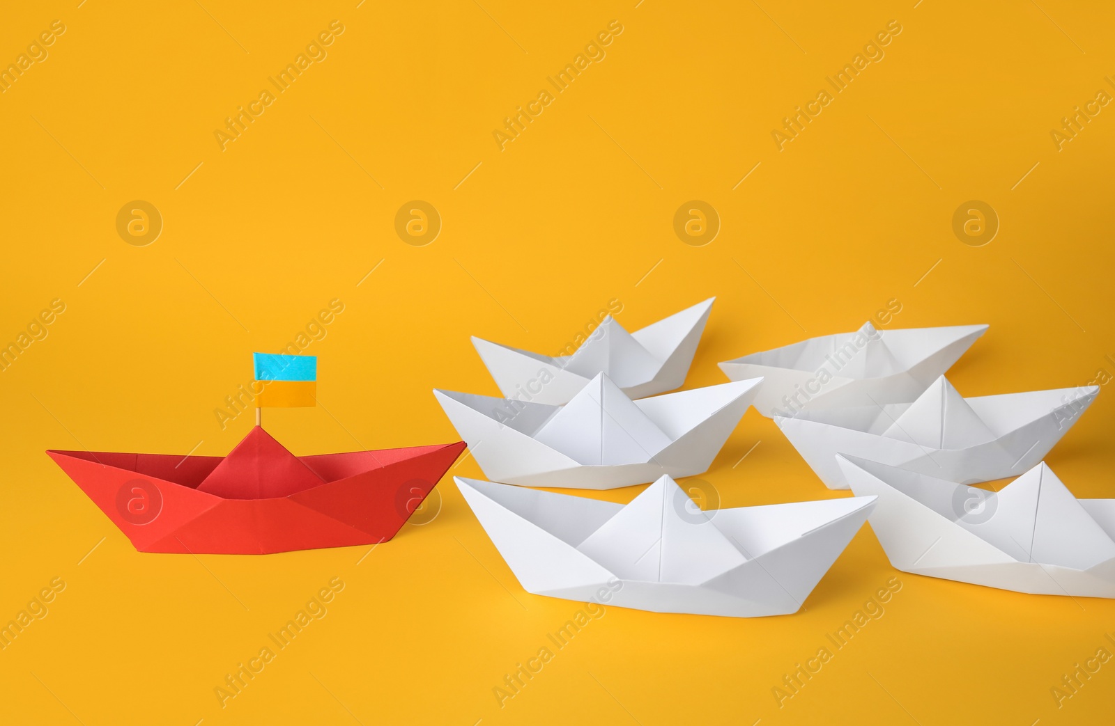 Photo of Group of paper boats following red one on yellow background. Leadership concept