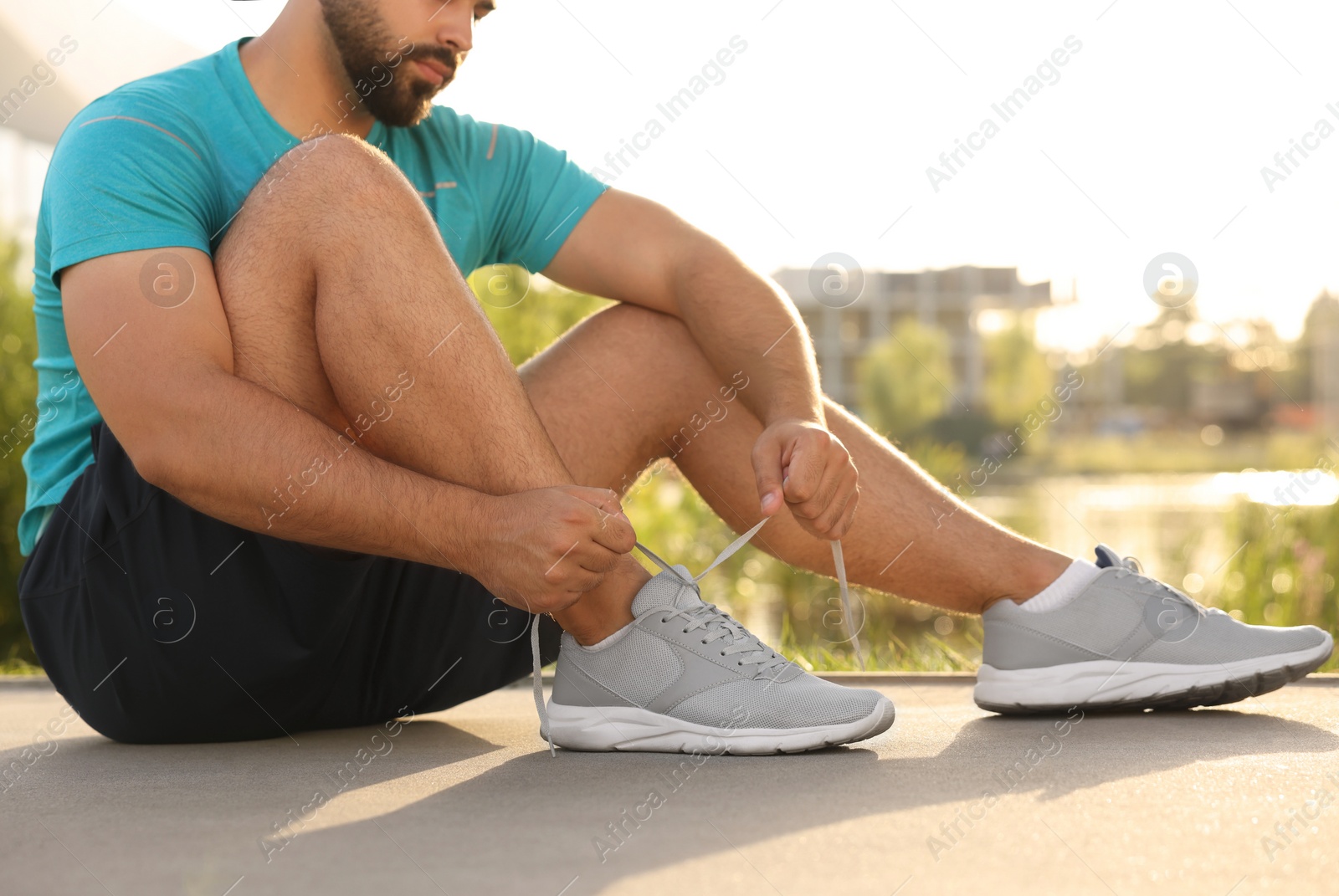 Photo of Man tying shoelaces before running outdoors on sunny day, closeup