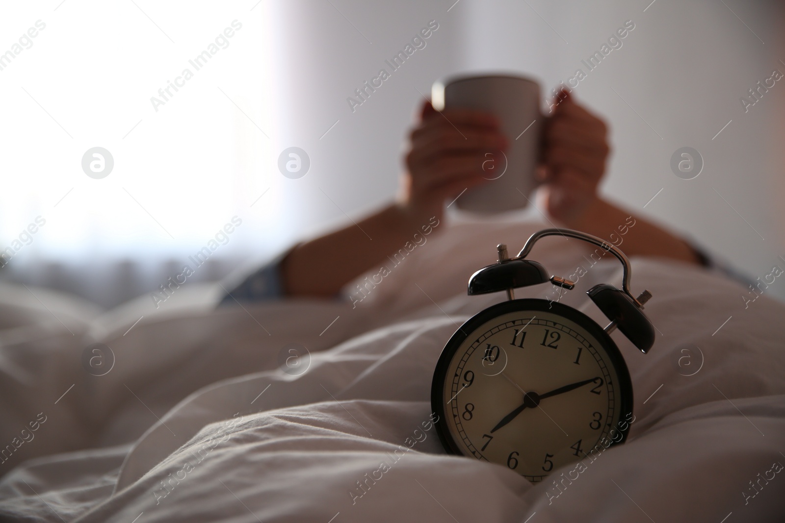 Photo of Woman with cup in bed, focus on alarm clock. Morning time